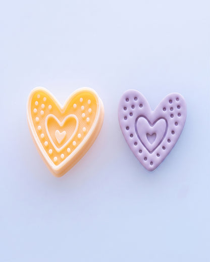 Close view of the Boho Dotted Heart cutter beside a matching purple clay imprint, showing the heart silhouette, dotted border and layered center detail.