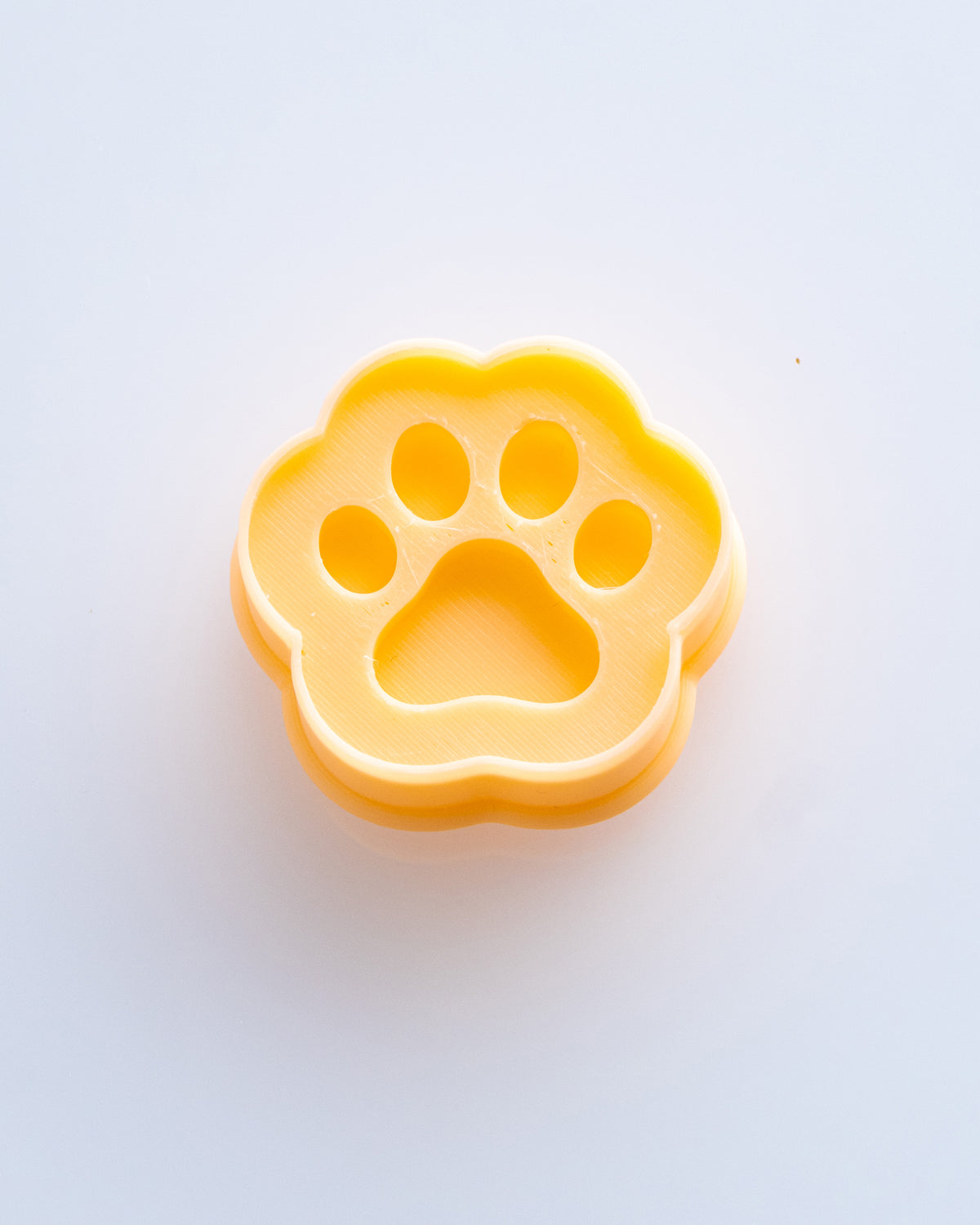 Close product view showing the printed Mini Paw Print clay cutter beside its matching polymer clay imprint.