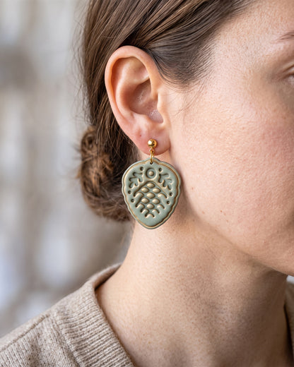 A model wearing finished Scandi Folk Pine Cone polymer clay jewelry, showing its appearance and scale when worn.